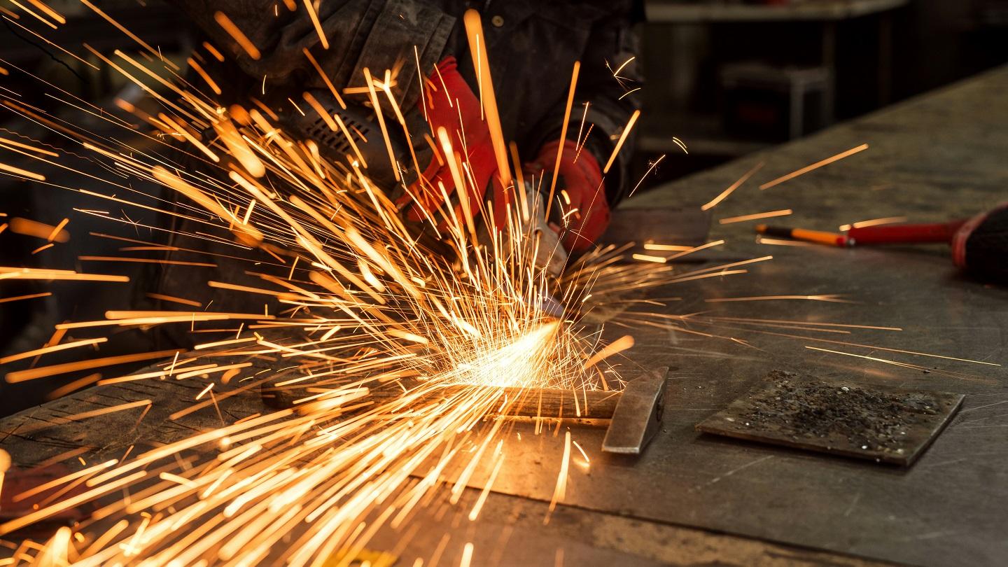 Man wearing red gloves angle grinding some metal, sparks flying