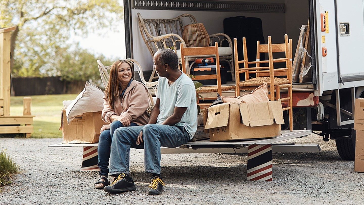 A couple sits outside their moving van.