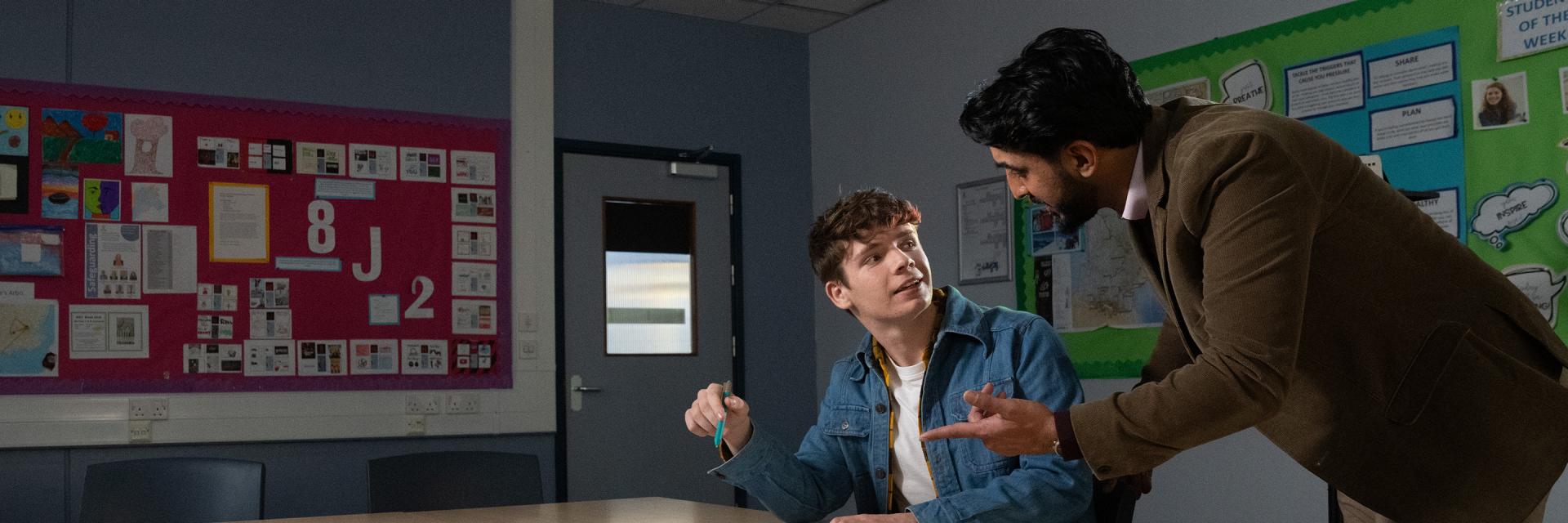 Student being helped by an older man within a classroom, illustrated by a glowing  'spark' 