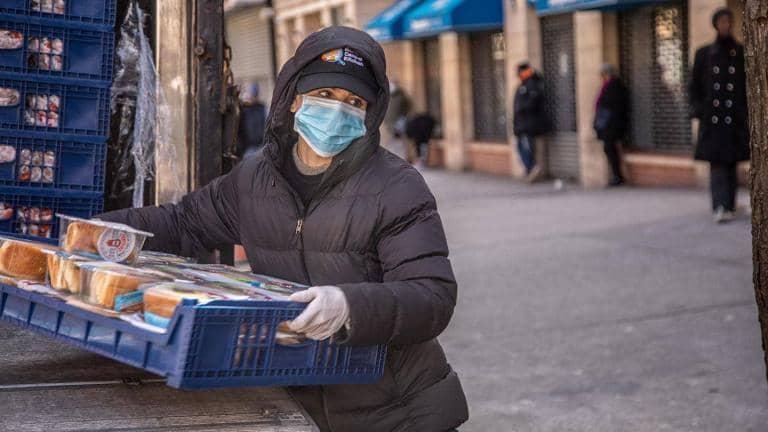 Person wearing face mask holding crate of food