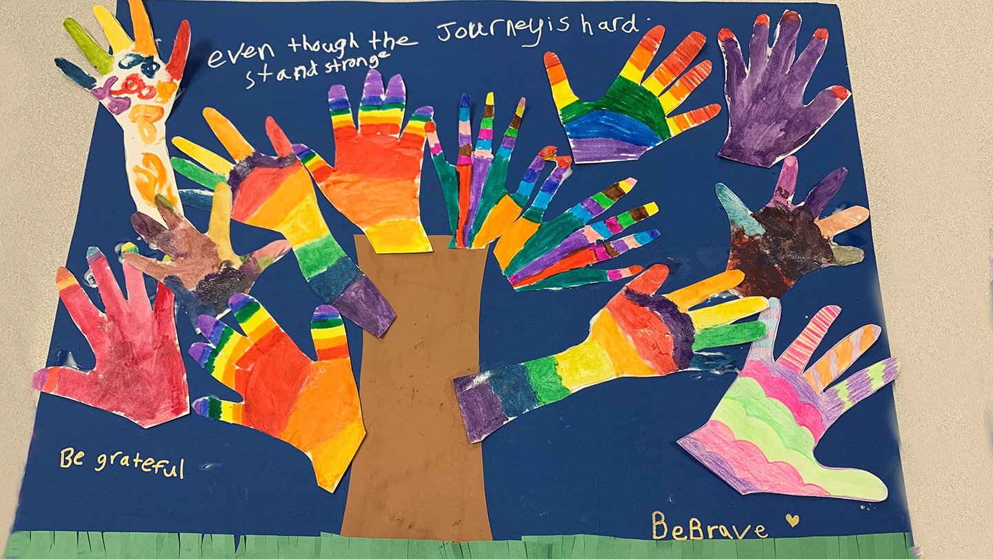 Children’s painted hands, glued in the shape of a tree to a poster.