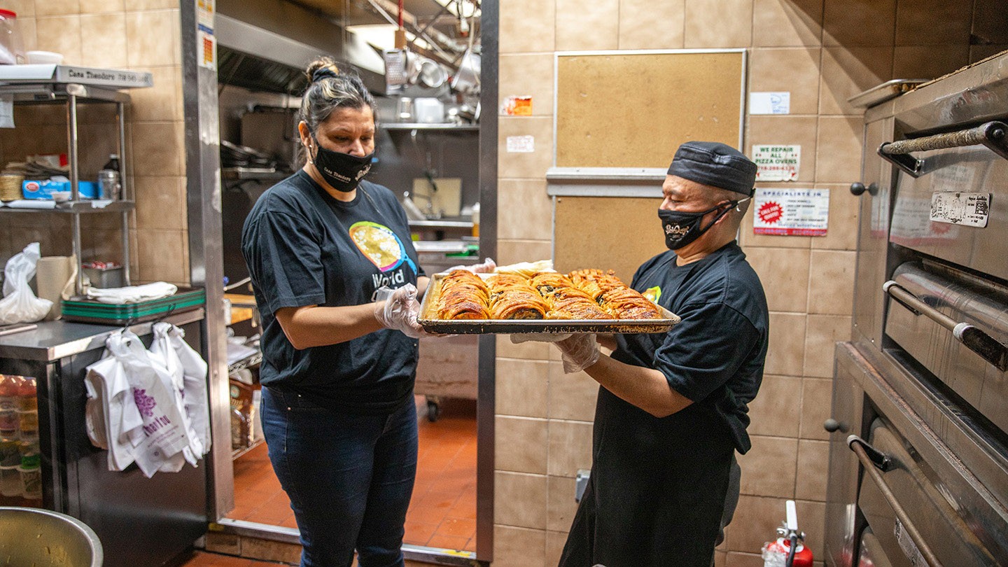Pao de Queijo workers handle a platter of food in the restaurant’s kitchen area.