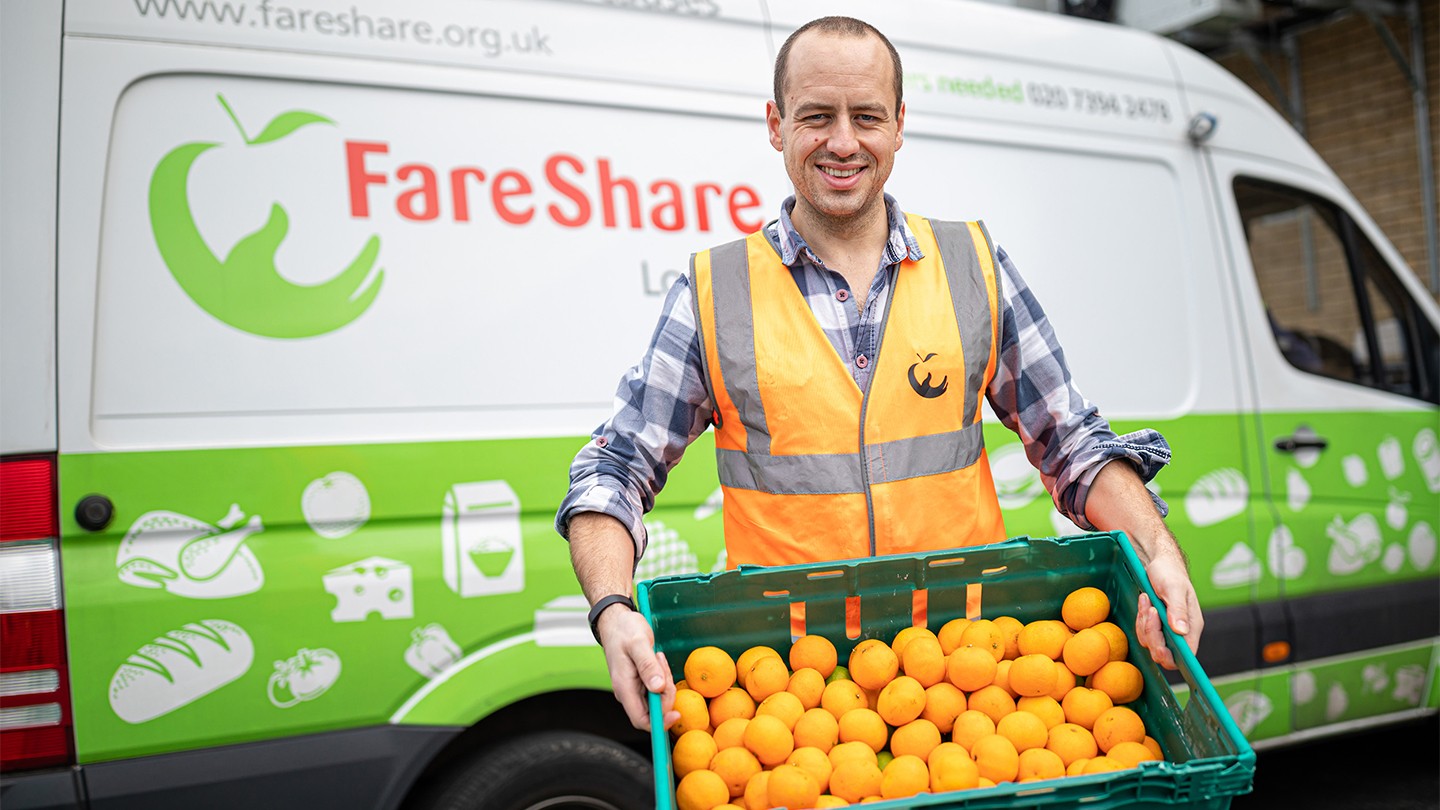 FareShare employee holding a crate of oranges
