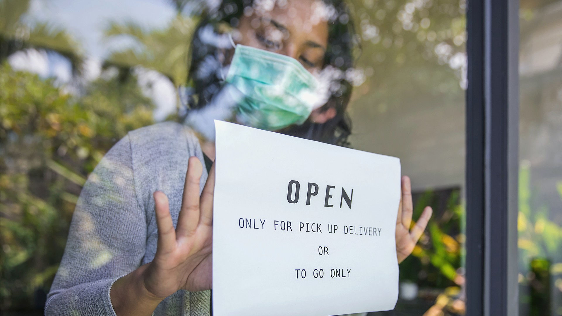 Business owner wearing a face mask and holding an 'open' sign