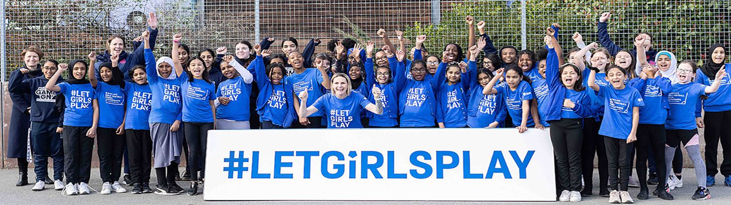 Kelly Smith MBE and a class of primary school girls pose in front of a sign saying 'let girls play'
