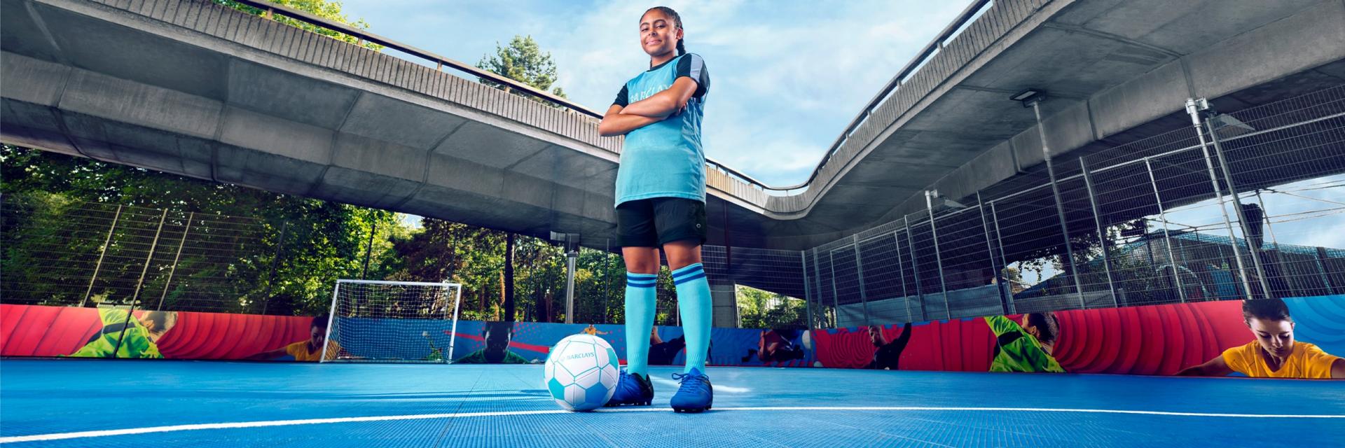 A girl in a blue Barclays bib, with a football.