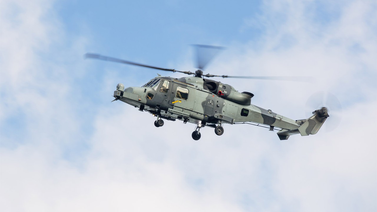Close up view of a military Wildcat helicopter practicing low flying and tactical stops over agricultural fields on the south coast of the UK with blue cloudy sky in the background.